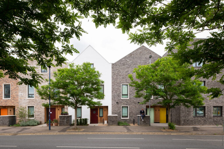 Street-facing view of Marmalade Lane co-housing in Cambridge, showing rows of terraced homes framed by trees.
