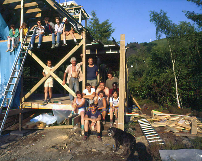 An ongoing self-build with a group of self-builders and their families posing in the structural frame of the house