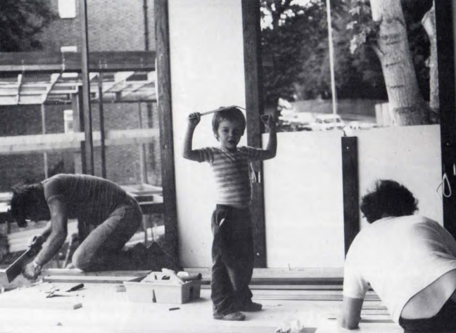 A self-build home under construction, a child playing with a ruler with two parents building on the floor either side